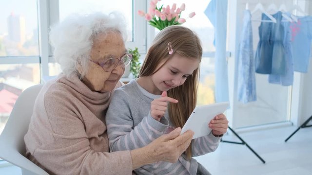Cute little girl teaching grandmother to use tablet sitting at home