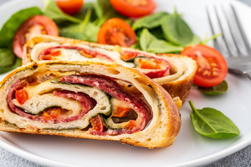 Italian food Pizza roll stromboli with cheese, salami, spinach and red pepper a light background.