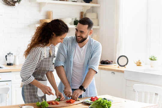 Couple preparing together vegetable salad standing in kitchen at home