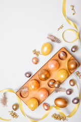 Top-down view of Gold colored Easter eggs in wooden stand with copy space for text on white background, flat lay design for Easter holiday