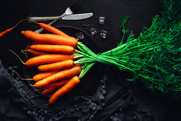 Fresh carrots on a black plate with ice. Food background for recipes and books