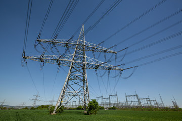 Power pylon with power lines and transformer station under blue sky in Germany