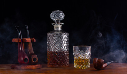 carafe and a glass of whiskey beside the smoking tubes standing on the table shrouded in smoke from...