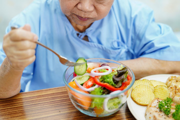 Asian senior or elderly old lady woman patient eating salad vegetable breakfast healthy food with hope and happy while sitting and hungry on bed in hospital..