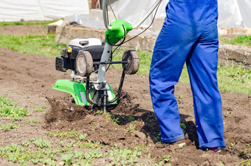 Young girl plows the land with a cultivator in spring garden