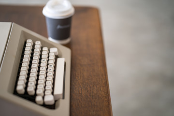 Cup coffee on wooden table next to vintage typewriter.