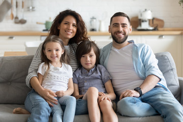 Happy family with kids seated on couch posing for camera