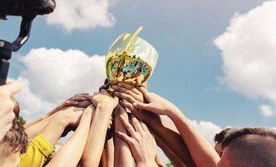 Kids in sports team lift up the golden cup trophy after winning the final tournament match....