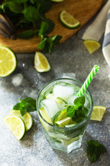 Fresh Mojito cocktail with lime, ice and mint in a glass on a gray stone background. Summer cold drink and cocktail.