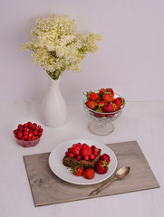 Festive dessert cupcake with strawberries and wild strawberries with copy space with a bouquet of white flowers. Valentine's Day. Birthday. Mothers Day. Vertical photo