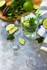 Summer cold drink and cocktail. Fresh Mojito cocktail with lime, ice and mint in a glass on a gray stone background. Copy space.