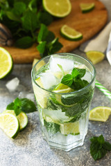 Summer cold drink and cocktail. Fresh Mojito cocktail with lime, ice and mint in a glass on a gray stone background.