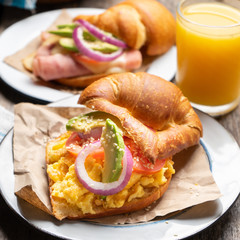 Butter croissant bread with scrambled eggs and avocado on wooden background