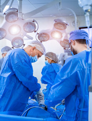 Group of doctors perform an operation to a patient. Surgeons in medical uniform and masks working in the operating room