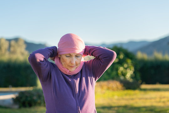 caucasian older woman putting a pink scarf on her head