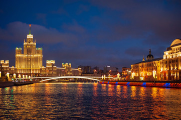 View of illuminated Stalin skyscraper on the festive illumination Kotelnicheskaya embankment and Moscow River at night in Moscow.