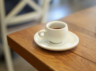 Espresso in white cup on wooden table in cafe.