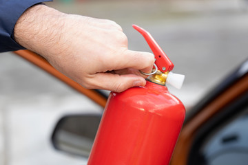 Naklejka premium Male hand pulling safety pin of fire extinguisher close up against the background of a car