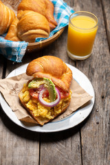 Butter croissant bread with scrambled eggs and avocado on wooden background