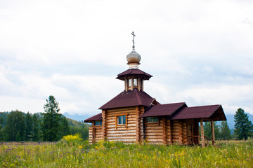 Small wooden orthodox temple in the mountains. Made from thick logs. Brown roof, cross on the dome