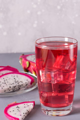 Glass of mango dragonfruit refresher drink on grey table with ice cubes. Copy space.