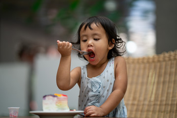 Cute asian girl eating multicolor cake.