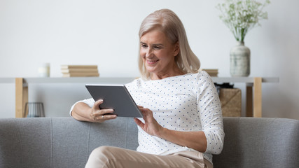 Modern elderly woman using tablet relaxing at home