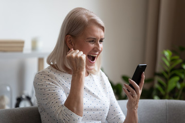 Excited mature woman feel overjoyed with good news on cellphone