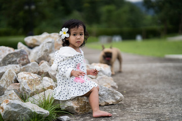 Cute little girl sitting on stone in park with her french bulldog.