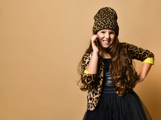 Young smiling plus size girl with long hair in leopard colored clothing and accessories standing and talking on her smartphone