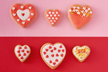 Decorated heart shape cookies on a colored red and pink background, top view