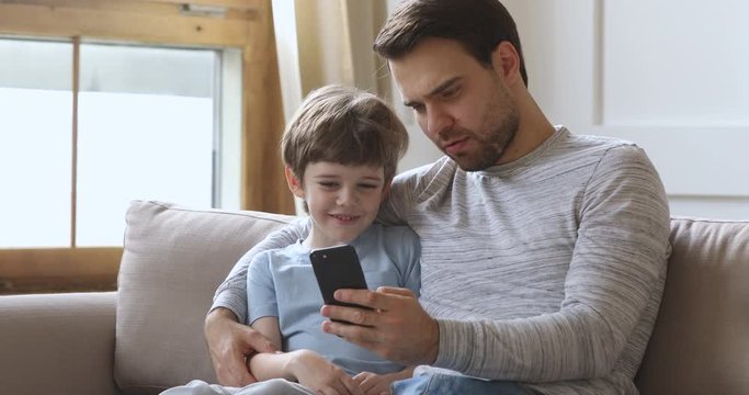 Dad teach kid son using phone having fun on sofa