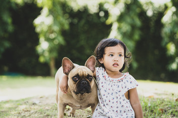 Cute girl sitting with her lovely french bulldog in park.