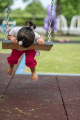 Cute little asian girl playing swing at playground.