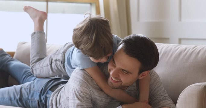 Son embrace father piggyback child looking at camera on sofa