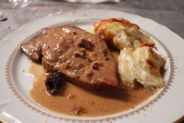 Rôti de veau aux morilles accompagné de gratin dauphinois - gratin de pommes de terre dans une assiette blanche