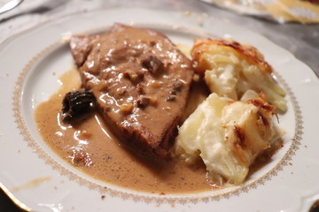 Rôti de veau aux morilles accompagné de gratin dauphinois - gratin de pommes de terre dans une assiette blanche