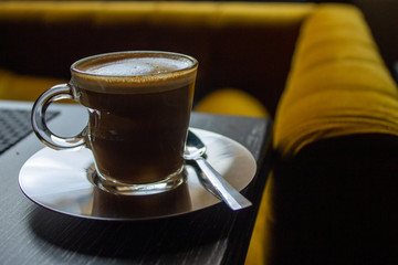 Cup of coffee next to mustard-colored sofa in warm and pleasant cafeteria.