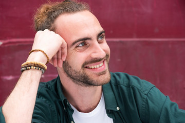 Close up smiling young man with beard looking away by red wall