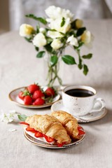 Breakfast in French. Croissant sandwich with I soft cheese and strawberries. And black coffee, a bouquet of flowers. Fresh strawberries. Soft focus. Space for text.  Copy Space