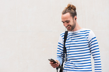 happy young man looking at mobile phone while listening to music with earphones by white background