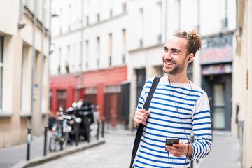 happy young man listening to music with smart phone and earphones in city