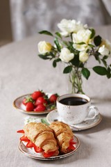 Breakfast in French. Croissant sandwich with I soft cheese and strawberries. And black coffee, a bouquet of flowers. Fresh strawberries. Soft focus. Space for text.  Copy Space