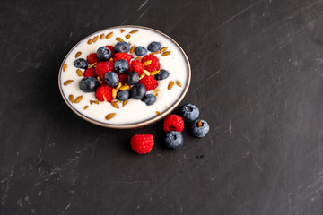 Tasty fresh blueberry raspberries  yoghurt shake dessert in ceramic bowl standing on black dark table background.