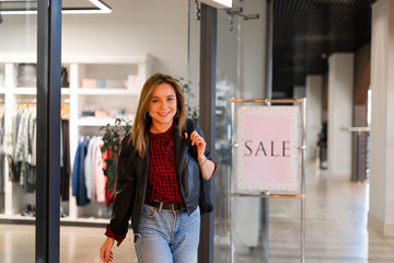 Young beautiful girl goes out clothing store with purchases. Season sale happy young adult female