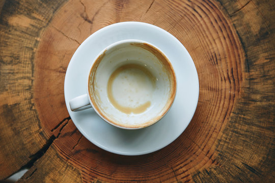 Top view of an empty white cup after drinking coffee on a wooden table. Concept for ending a meeting or something else.