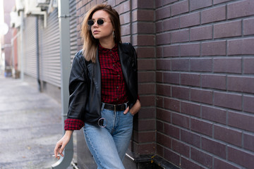 Beautiful young stylishly dressed Caucasian girl smokes cigarette on the street.