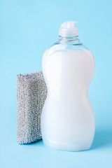 White dishwashing liquid in a transparent plastic bottle and silver foam sponge. Purity and household chemicals. Kitchen detergent. On a pastel blue background.