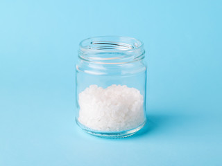 Large white crystals of sea salt in a glass bottle on a pastel blue background. Natural food spices and seasonings. Healthy eating.