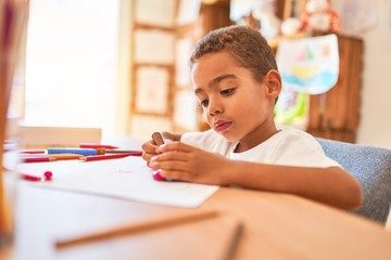 Beautiful african american toddler sitting painting car toy using marker pen on desk at kindergarten